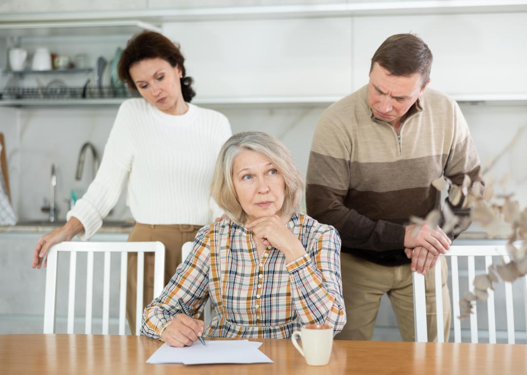 A senior woman signing documents with adult children behind her.