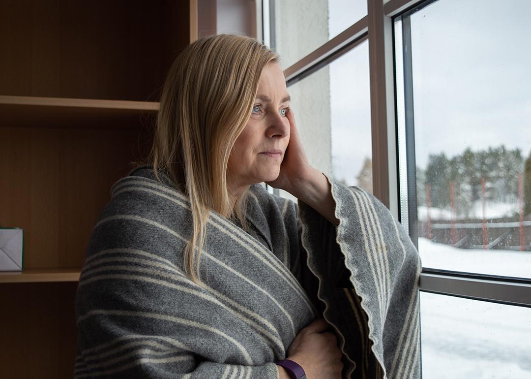 Woman wrapped in blanket looking out the window during winter.