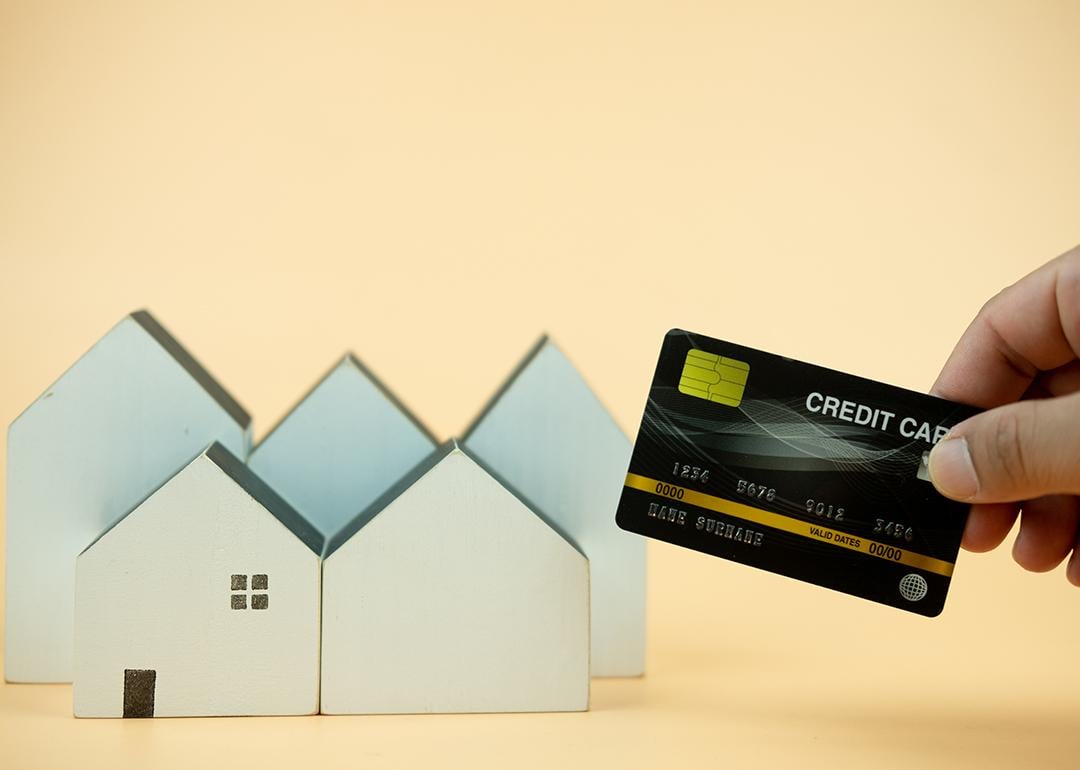 Hand holding a credit card over small figures of houses.
