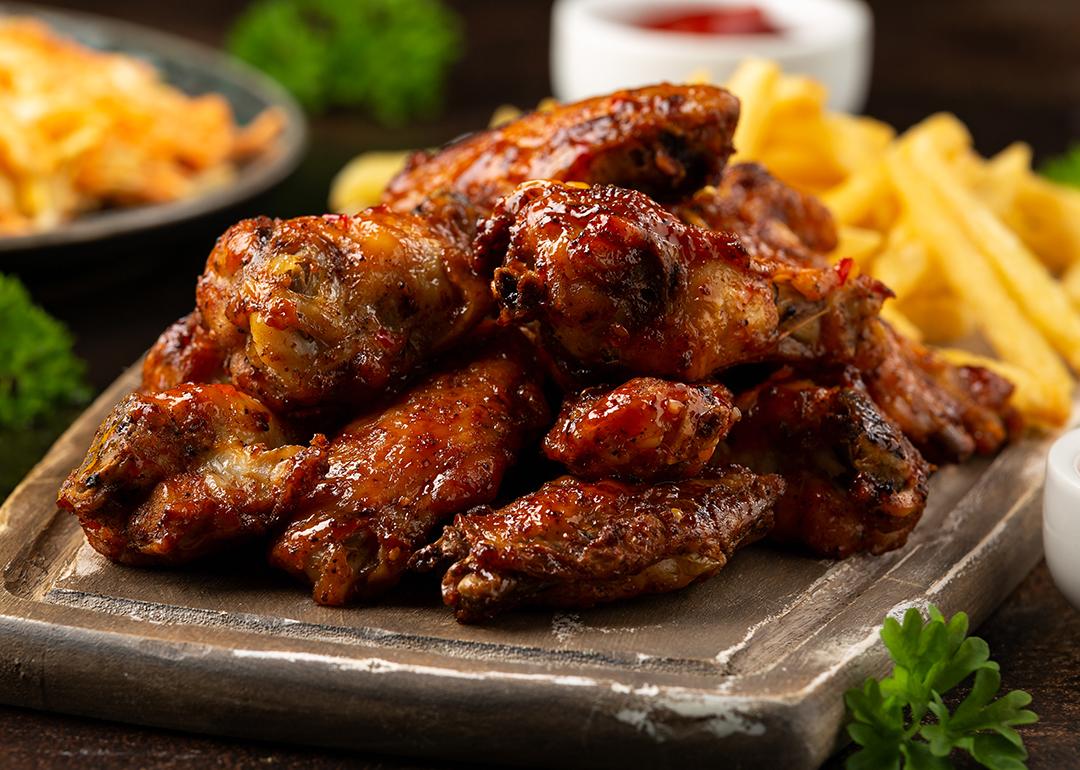 Buffalo chicken wings served on a wooden board with fries and other side dishes.