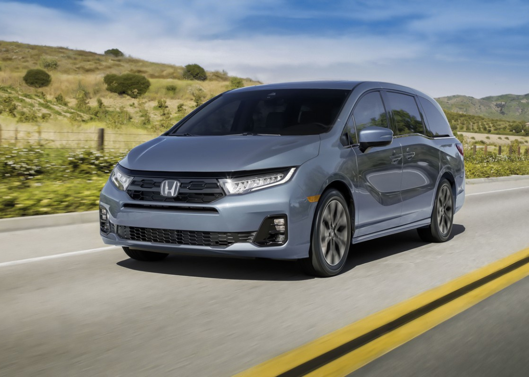 A dark gray Honda Odyssey driving down a rural road. 