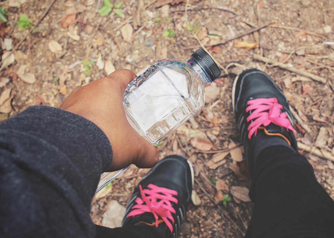 A selfie-style photo showing a person holding a water bottle and their fitness shoes while outdoors.