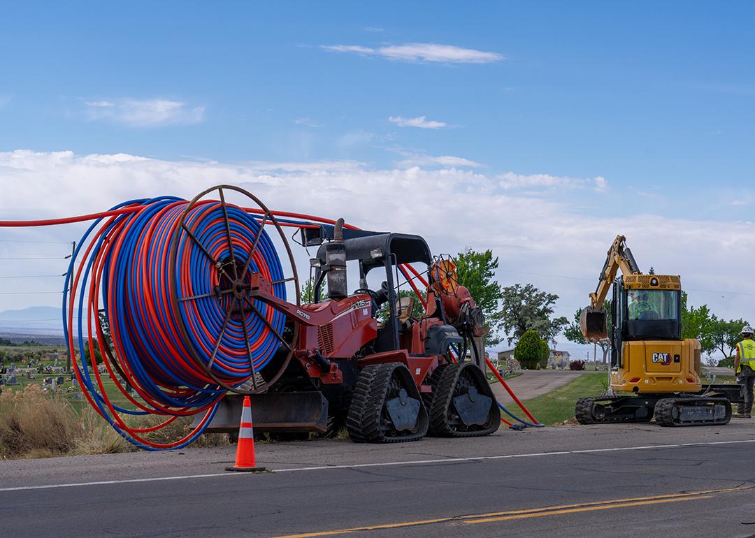Machinery vehicles parked on roadside while installing internet fiber optic cables' plastic conduit underground in a rural area in Utah.
