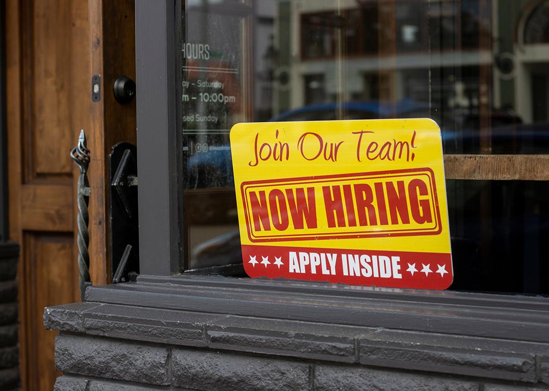 A 'now hiring' sign displayed on a glass window.