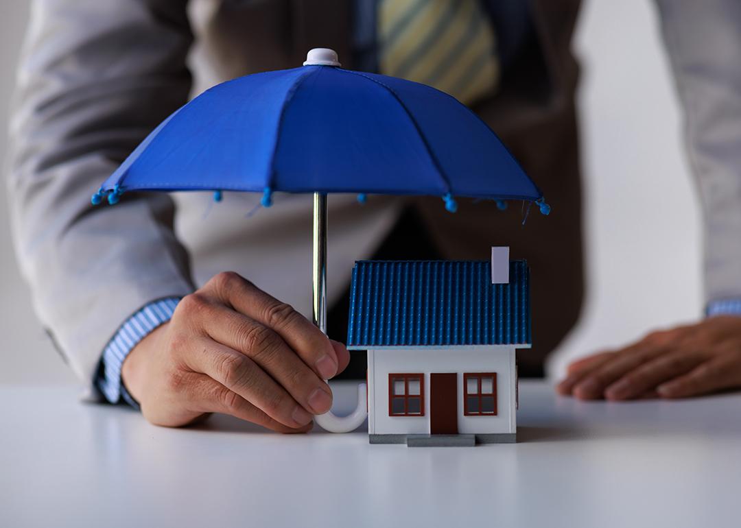 A figure of a house with a person holding small umbrella over it as a concept of home insurance.