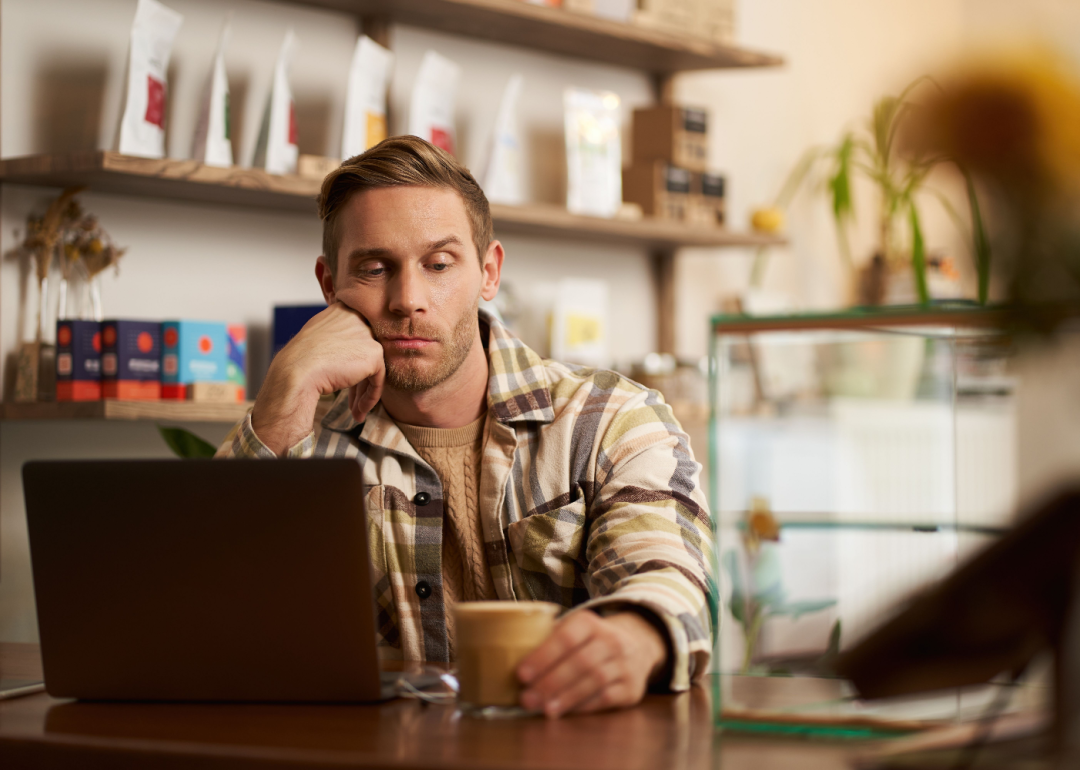 Man glumly staring at his laptop in a coffee shop.