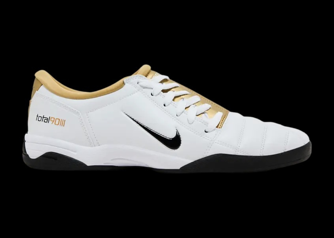 A pair of mostly white soccer shoes with a black Nike swoosh and a gold lining.