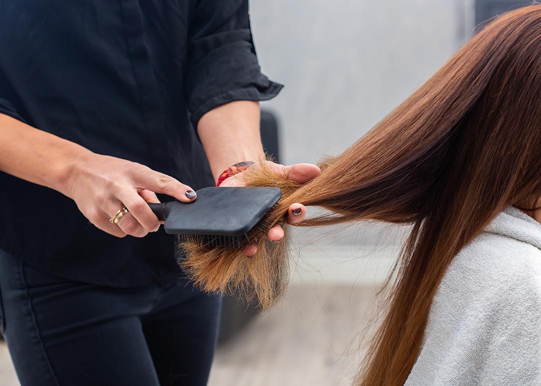 A professional hairstylist combing a client's hair with a paddle hairbrush.