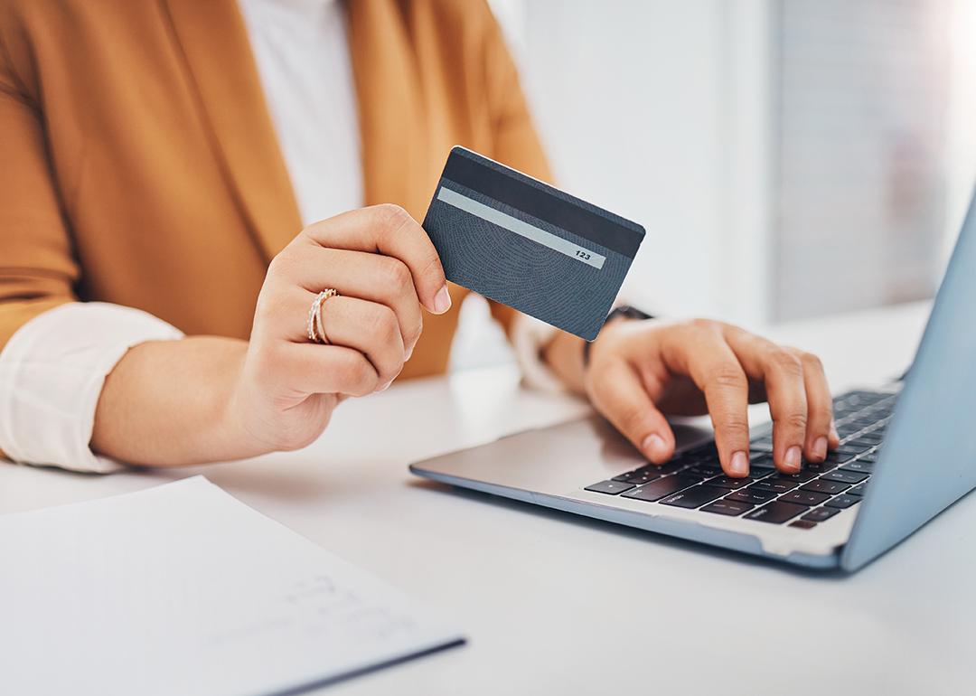 Person holding a credit card while using a laptop.