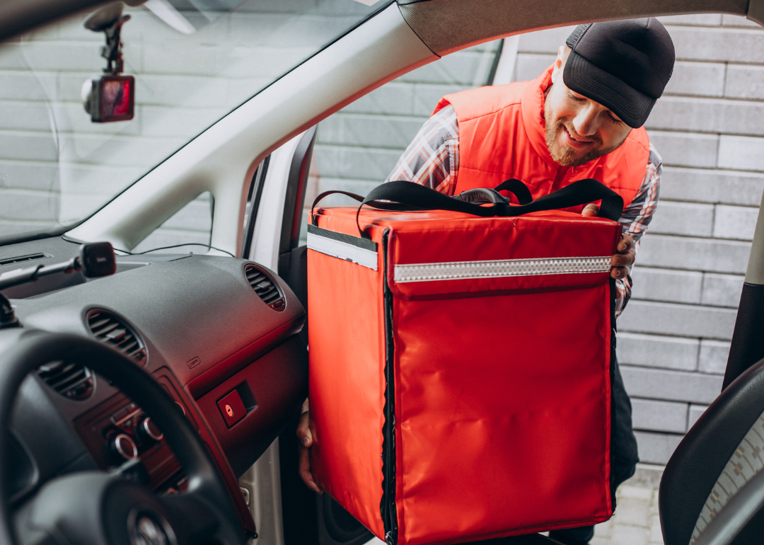 A food delivery person putting zipping up his delivery bag in his car.
