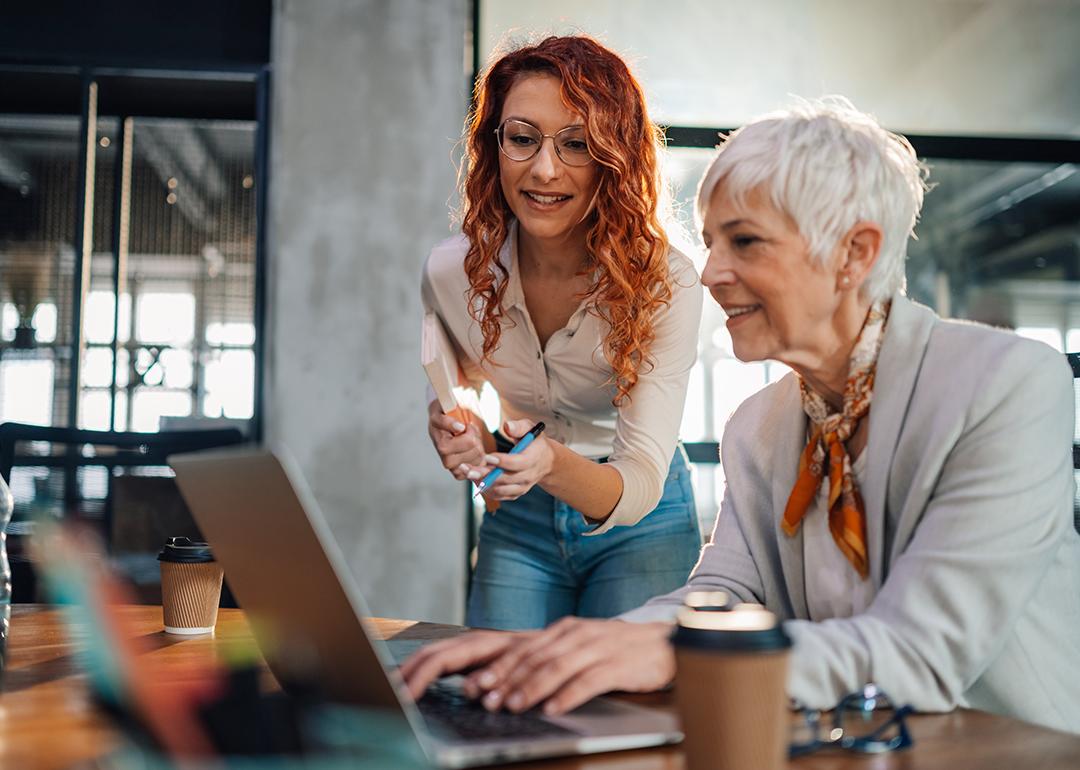 A senior employee working with a younger colleague on a task in an office.
