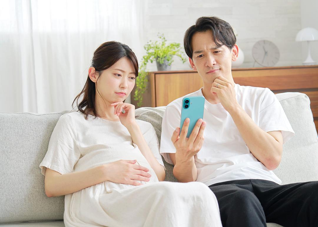 A pregnant wife and her husband curiously browsing information on a smartphone while sitting on a sofa at home.