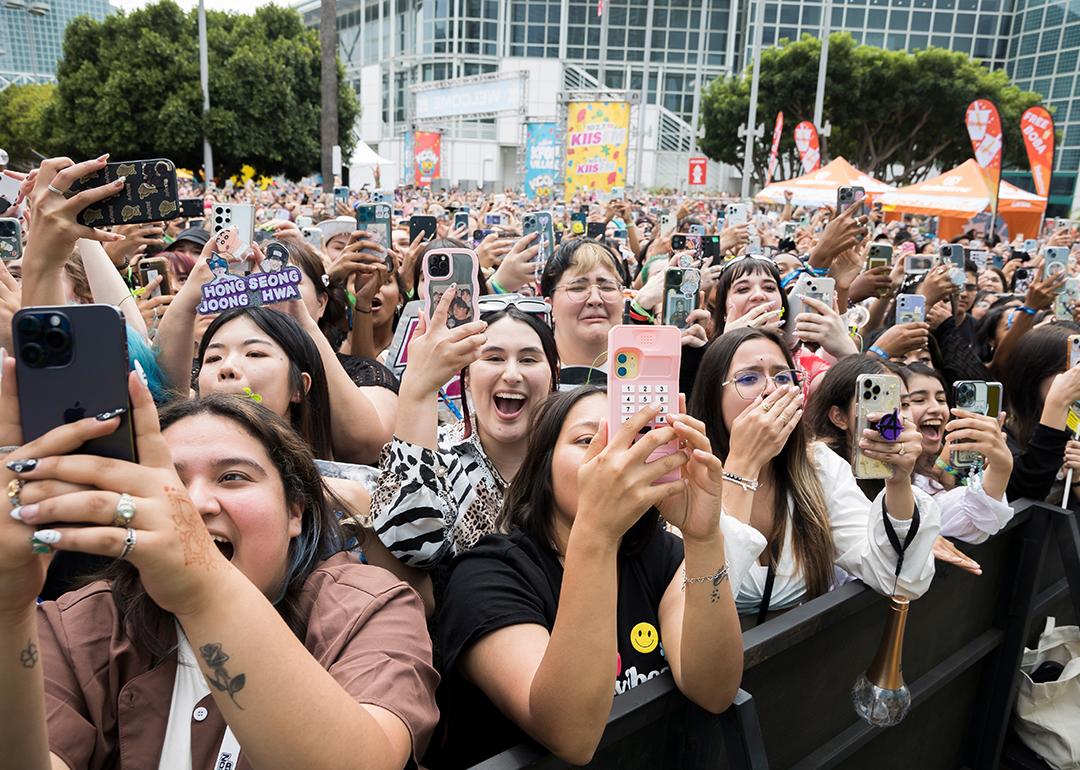 A crowd of fans holding their phones up and cheering outside the Crypto.com Arena for a K-Pop concert in Los Angeles, California.