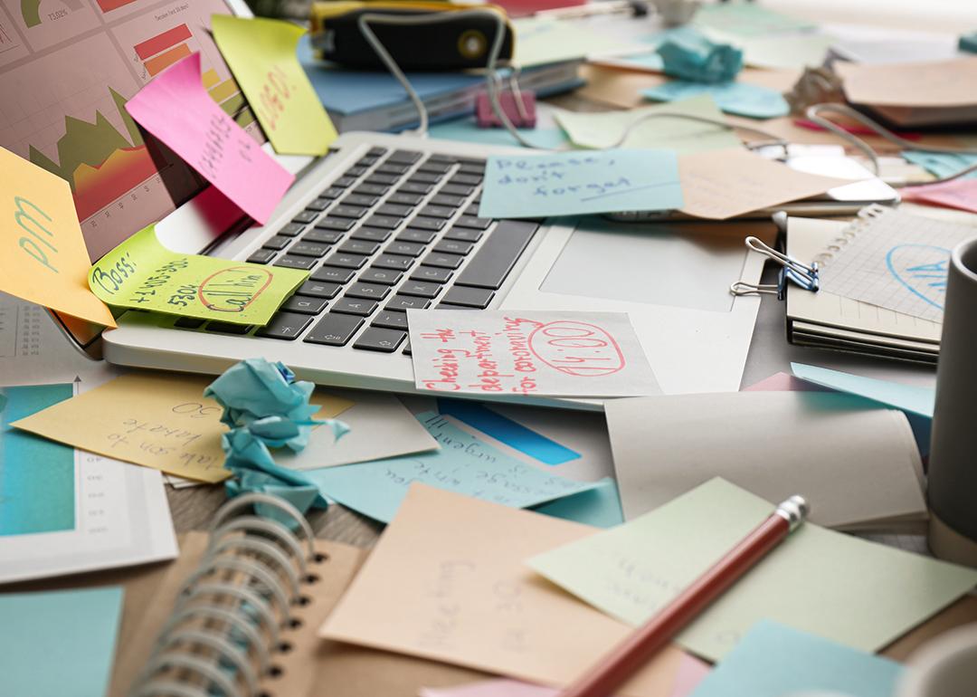 Sticky notes mess on top of a laptop on a working desk.