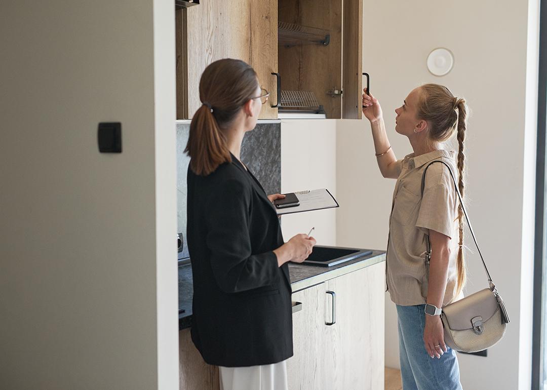 A young woman checking cabinets of an apartment with a female real estate agent.