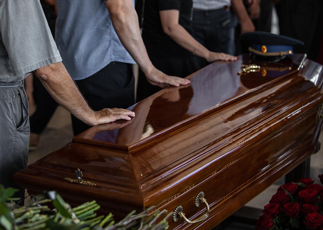 People touching the wooden brown coffin of a deceased relative.