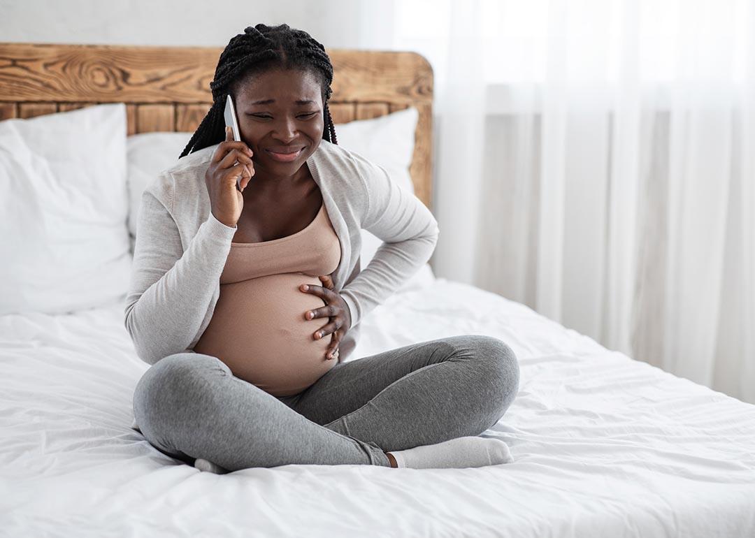 A pregnant young black woman calling on the phone while experiencing pain in her belly.