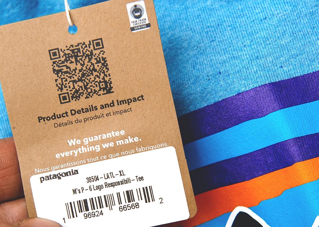 A product tag on a blue clothing shirt with QR code for product details and impact.