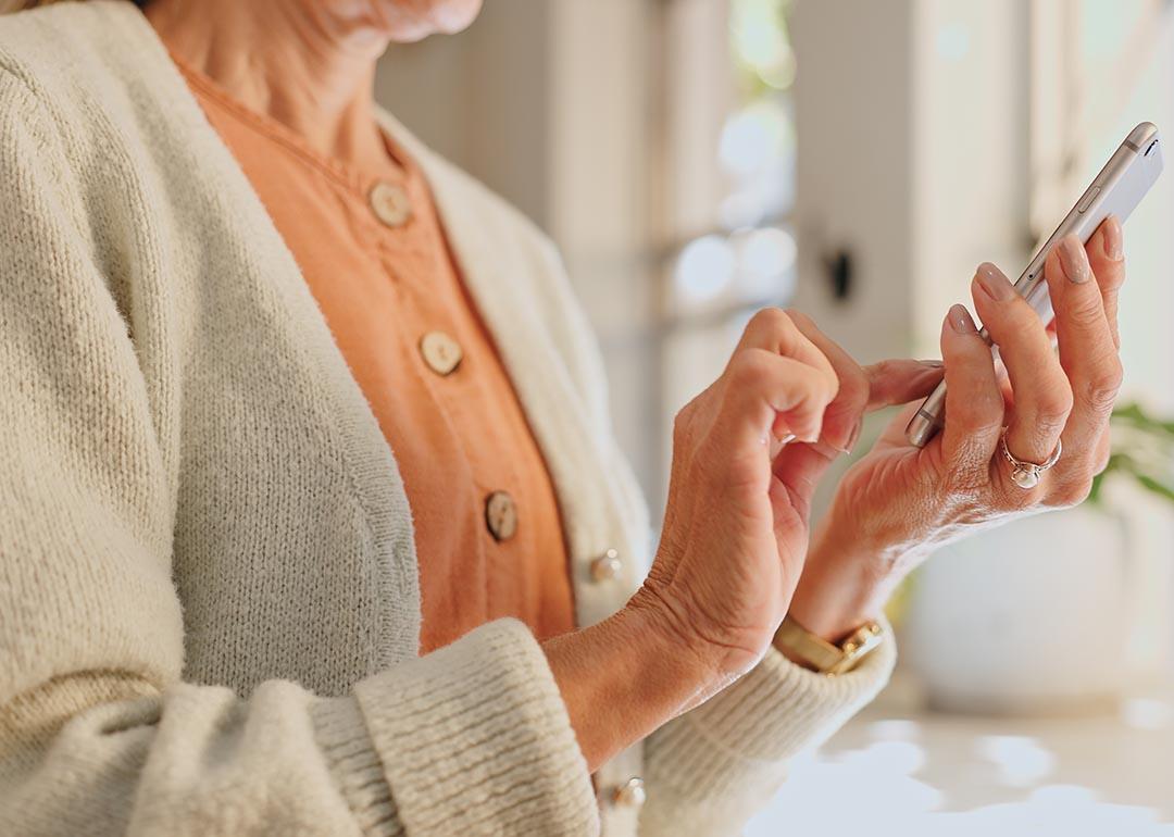 Older woman wearing a peach sweater texting on her phone