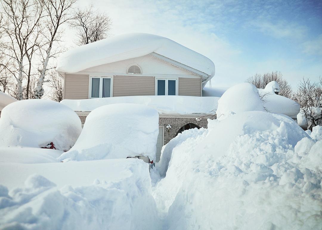 A house and its cars covered in deep white snow after a blizzard.