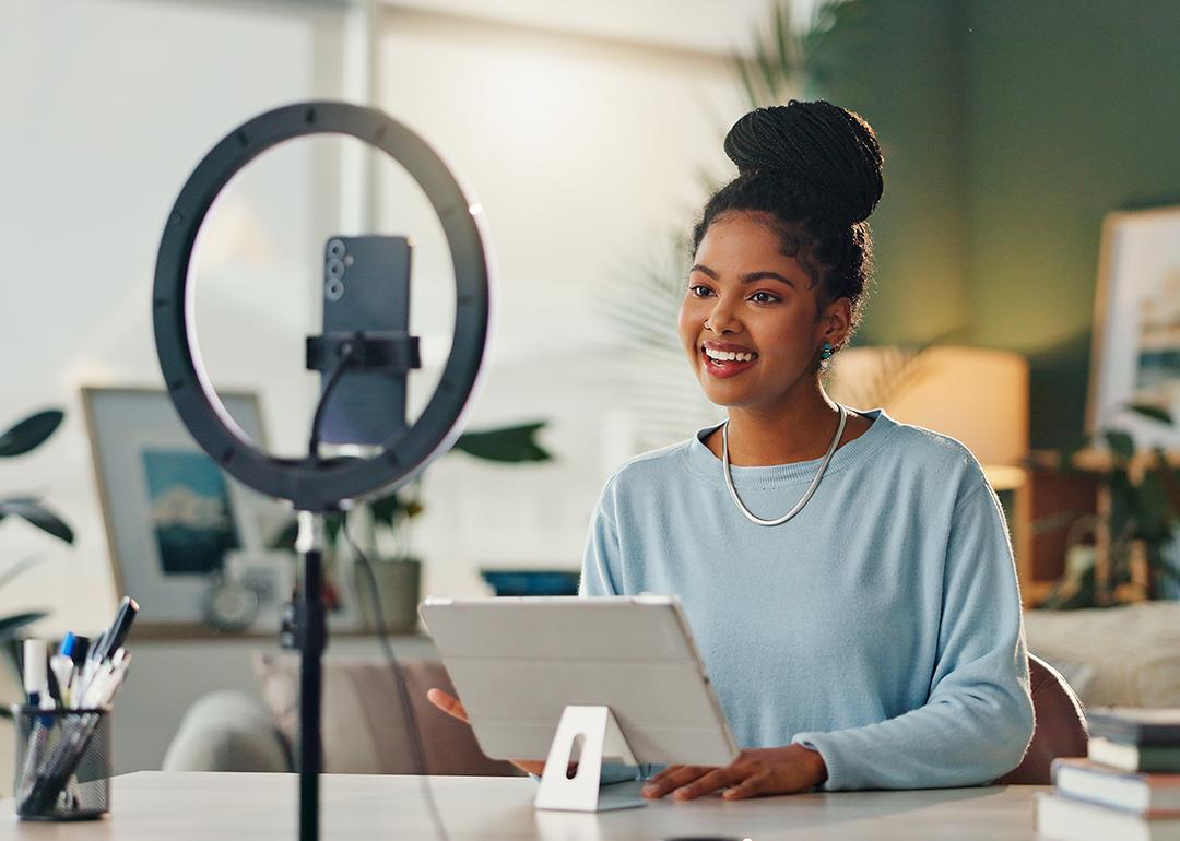 A young woman filming vlog content at home using her smartphone and a tripod.