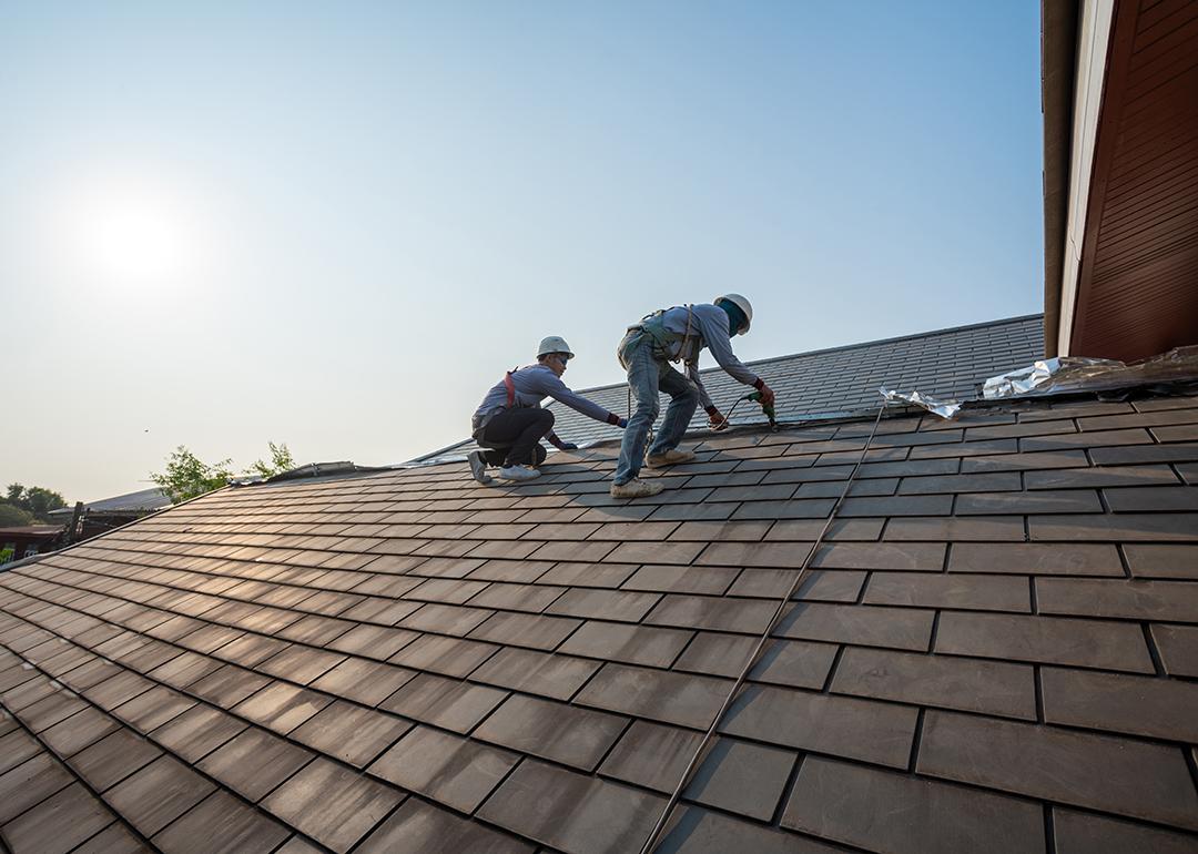 Two roof workers in full gear as they replace tiling on a roof.