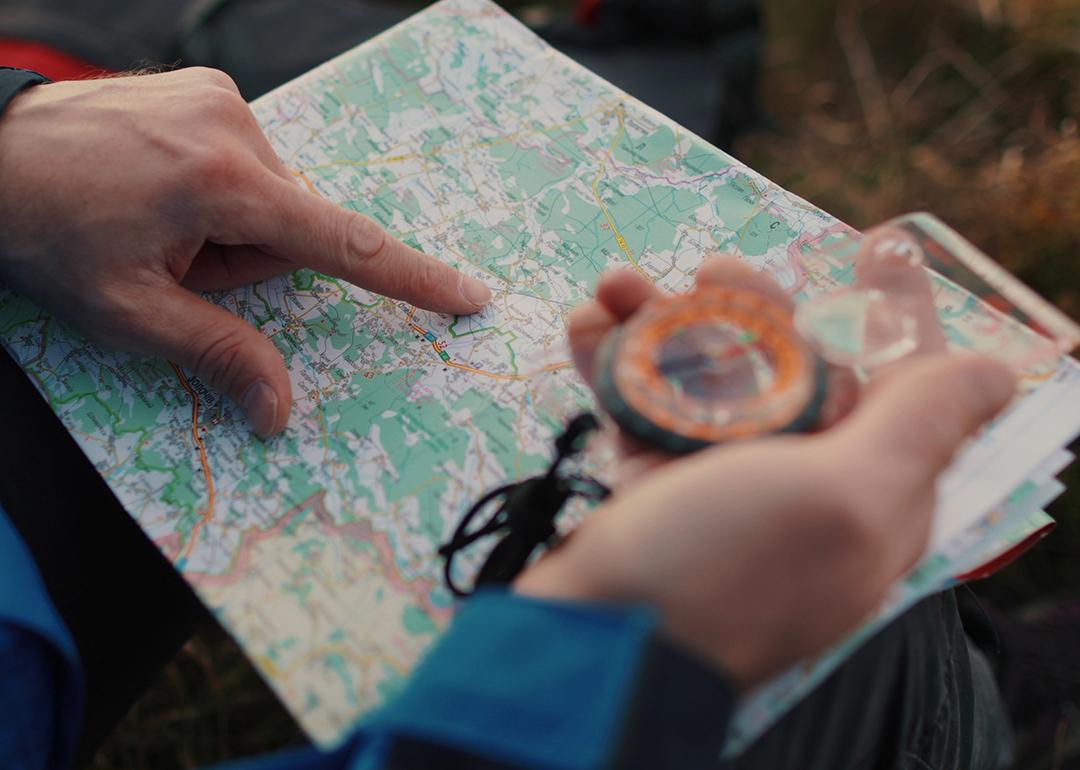 Close up on a traveler's hands navigating a trail map and compass.