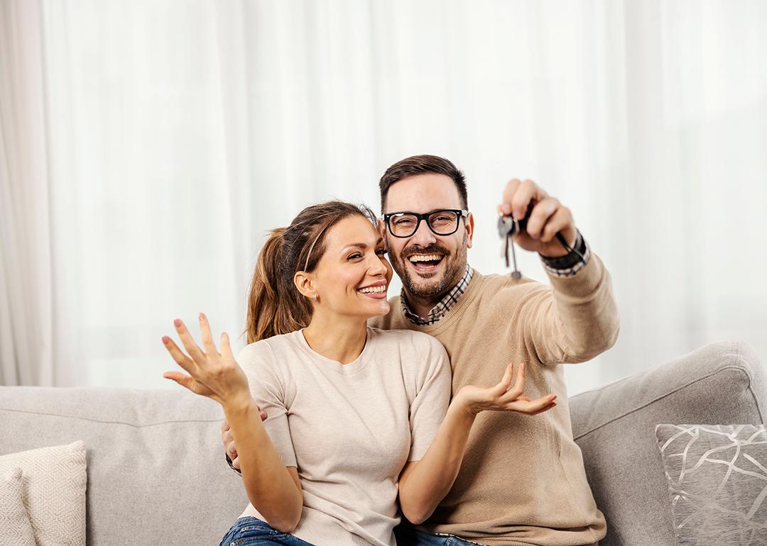 A happy couple taking a photo and showing off their new home's keys to the camera.