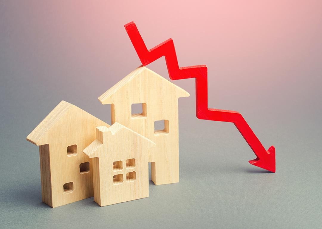 Figures of wooden homes and a red declining arrow as a concept of decline in real estate.