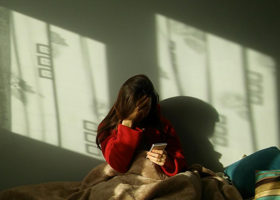 A sad woman in bed making a call on her phone.