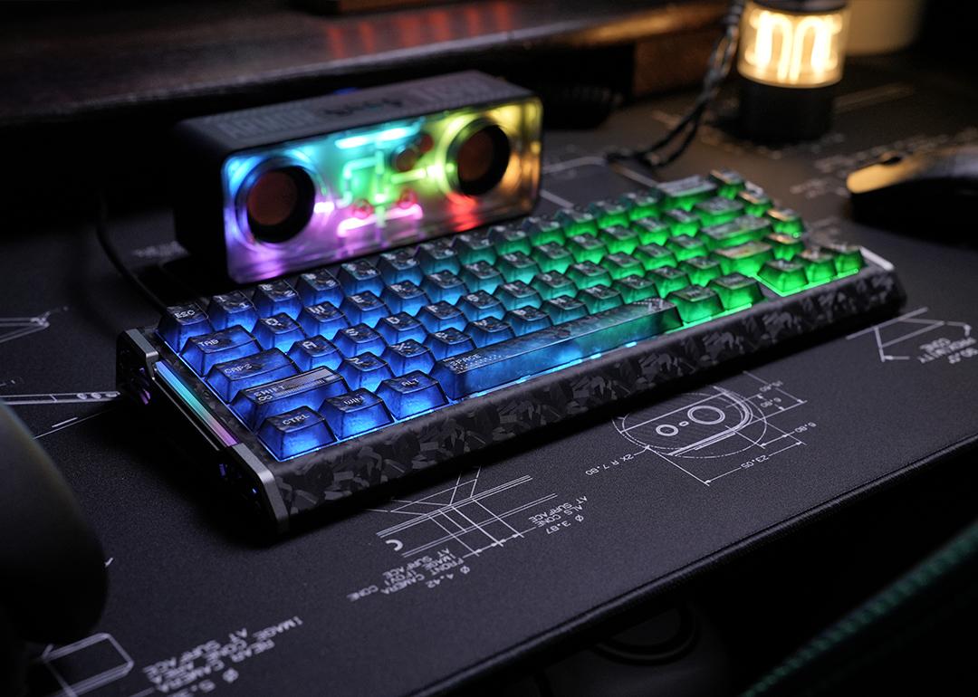 A blue-lit mechanical keyboard and a rainbow-colored speaker on a desk.