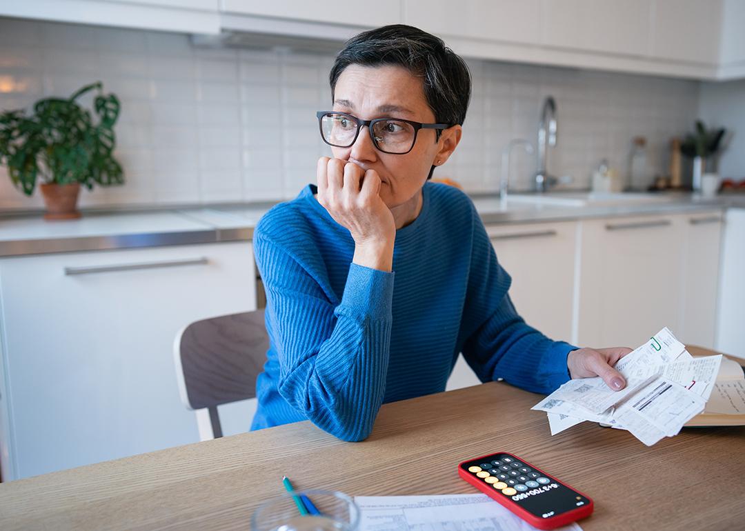 A stressed middle-aged woman looking away from bills at home.