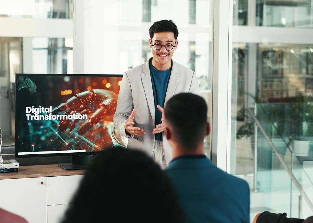 A young male public speaker giving a talk about digital transformation to a group of corporate employees at a conference.