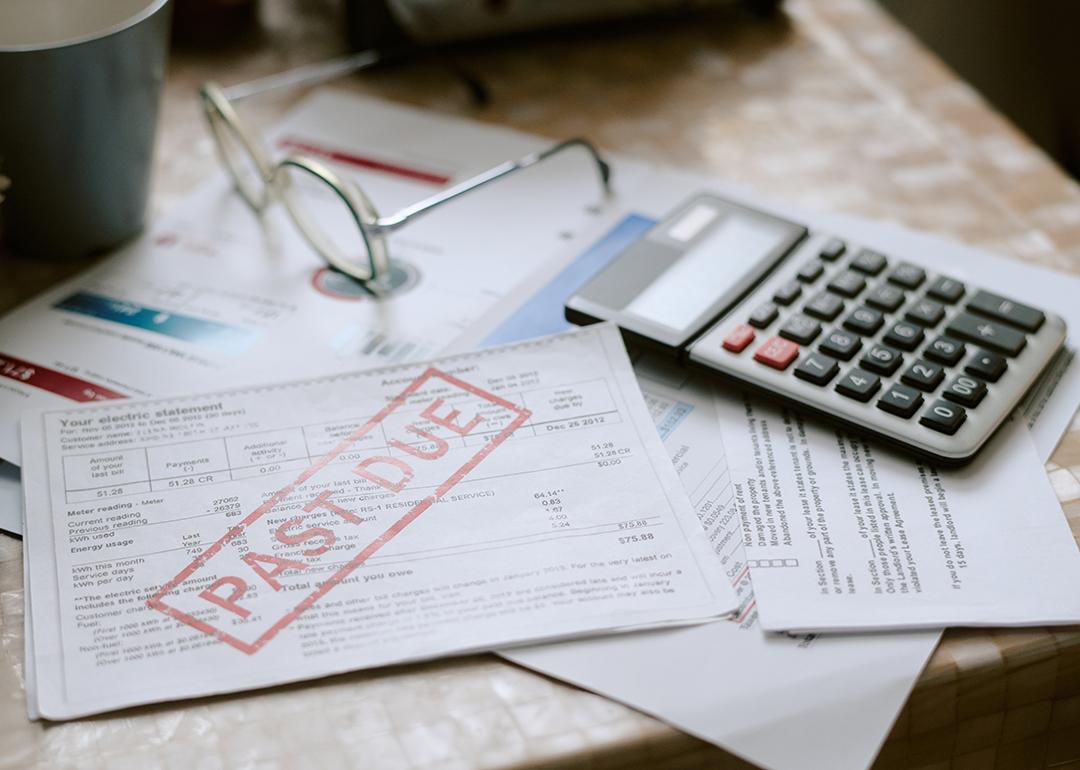 Bills stamped with a past due sign beside a calculator on top of a desk.