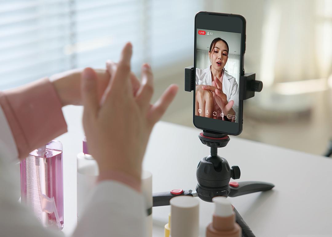 A female vlogger filming a skincare product review using a smartphone on a tripod.