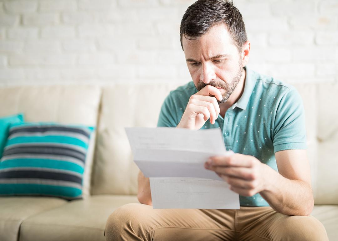 A man at home pensively looking at a debt document.