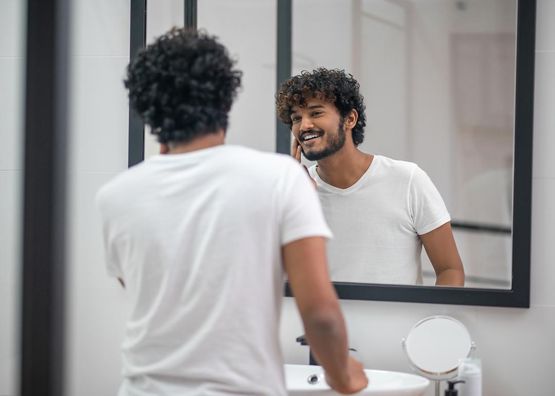 A young man looking at the mirror being pleased with himself.