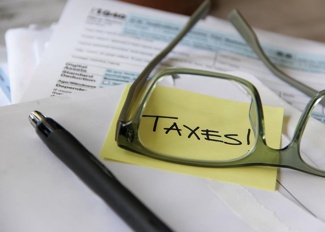 A low-angle view of tax documents and the word 'Taxes' written on a yellow sticky note viewed through eyeglasses.