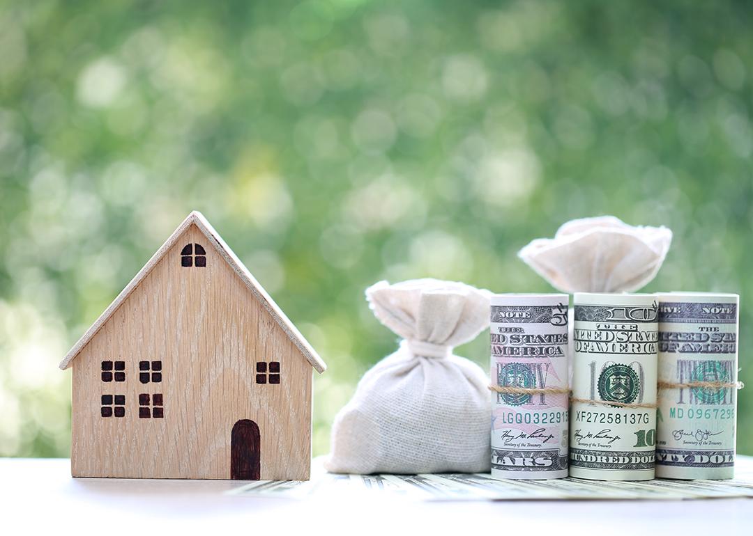 A wooden figure of a model house with banknotes on the side as a concept of saving money for a home.