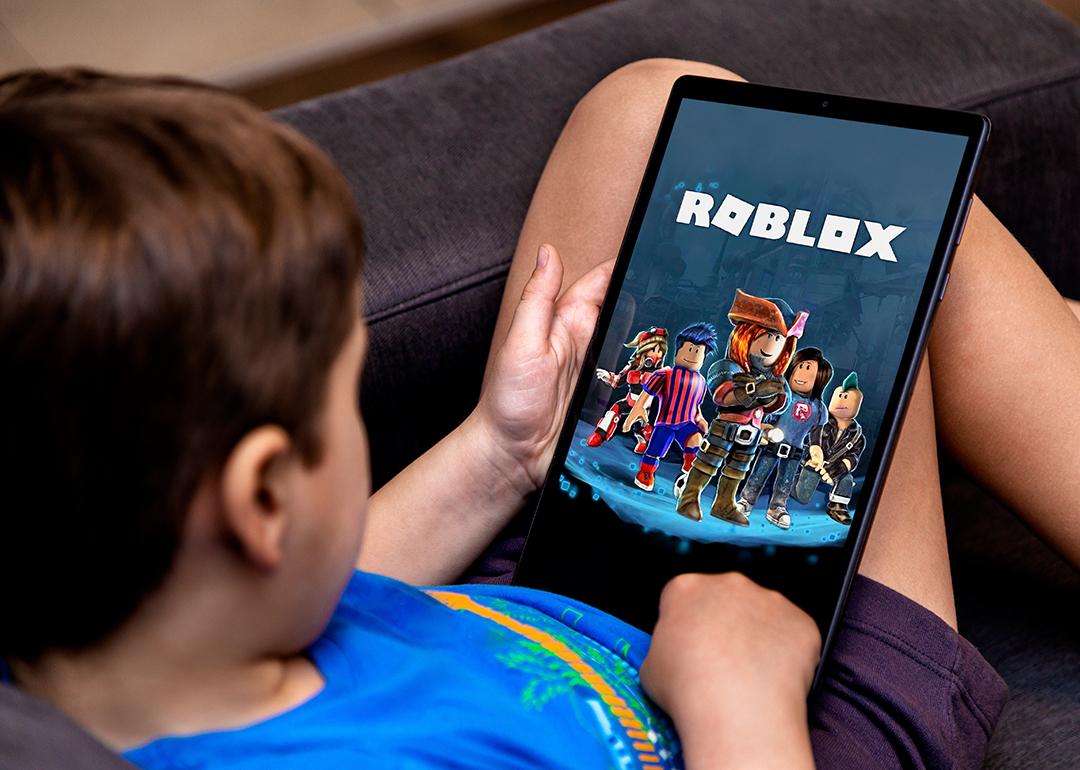 A young child sitting on a sofa and playing Roblox using a tablet.