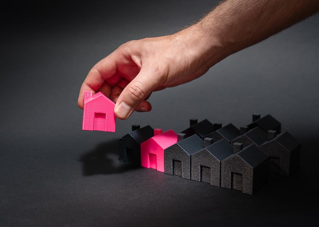 Figures of pink model houses being lined up with a row of black houses as a concept of national housing supply.