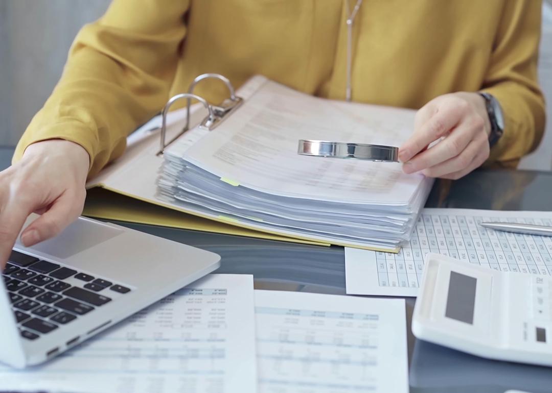 An auditor reviewing financial reports using a magnifying glass.