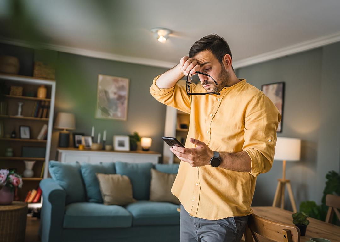 A man at home stressfully looking at his smartphone.