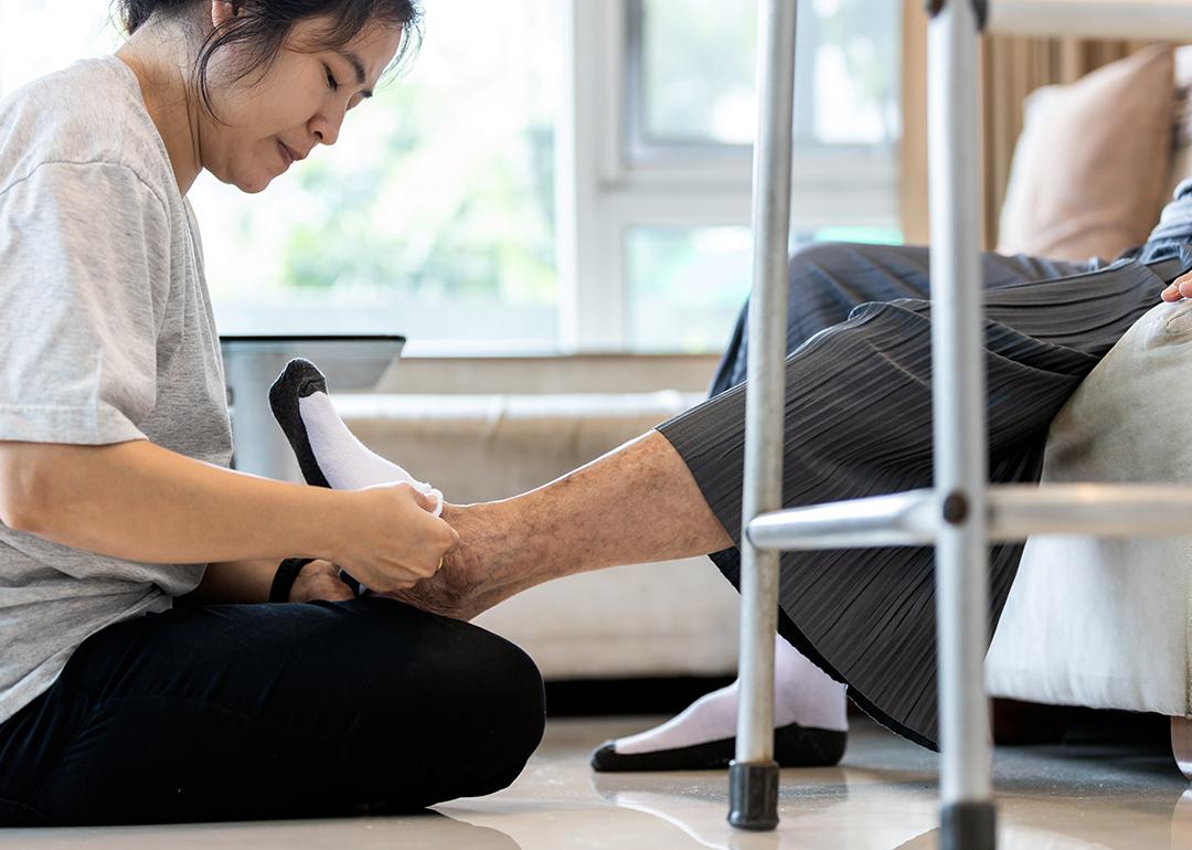 A female caregiver helping a senior person to wear socks at home.