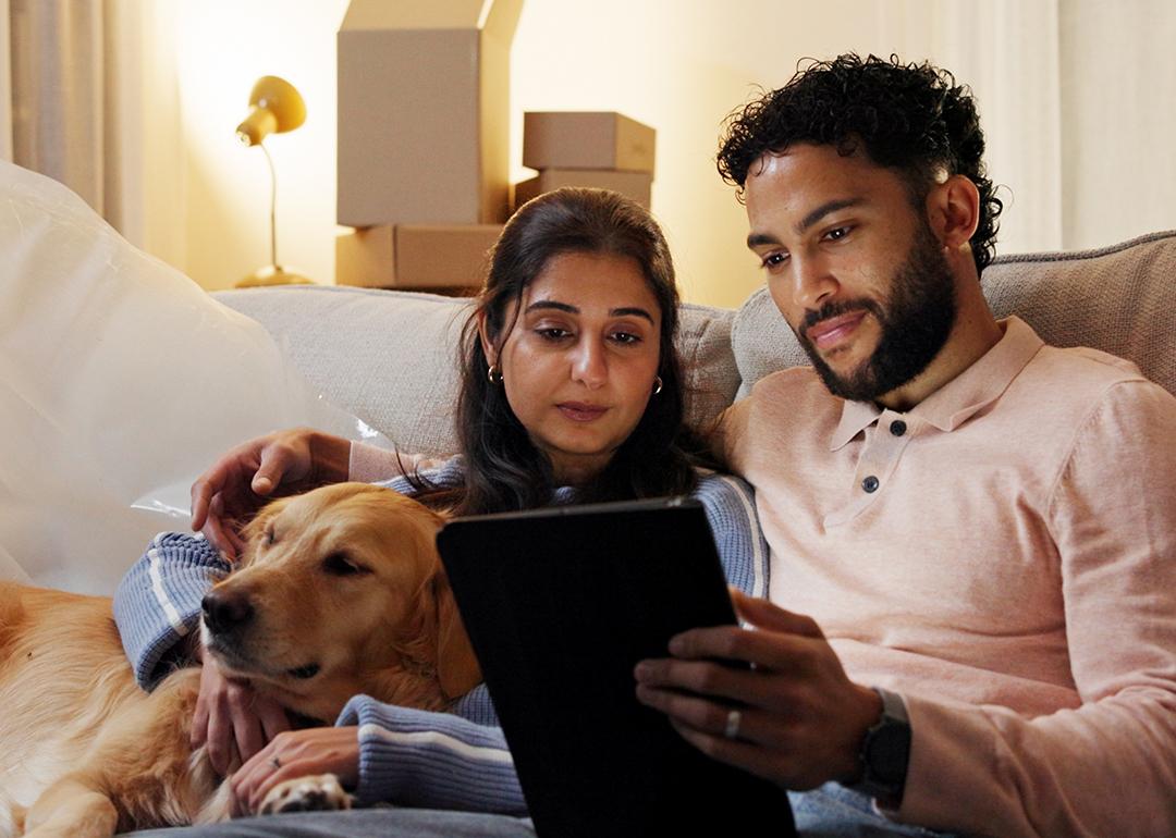 A couple with their dog relaxing in their new home and watching from a tablet.