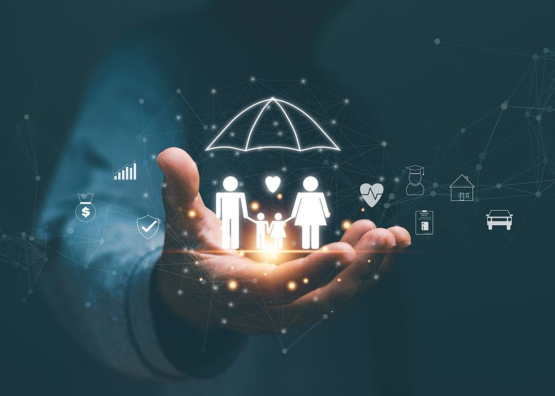 Person's hand holding hologram graphics of a family with an umbrella as a concept of life insurance.