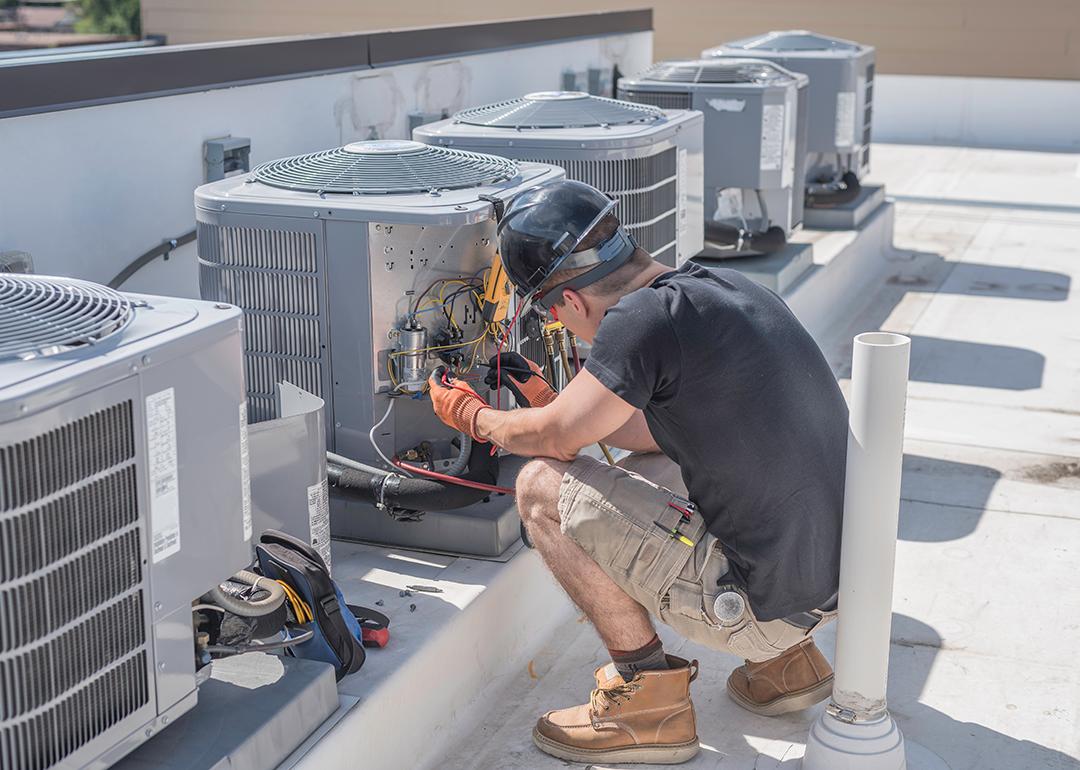 An HVAC tech at a rooftop checking a condenser unit.