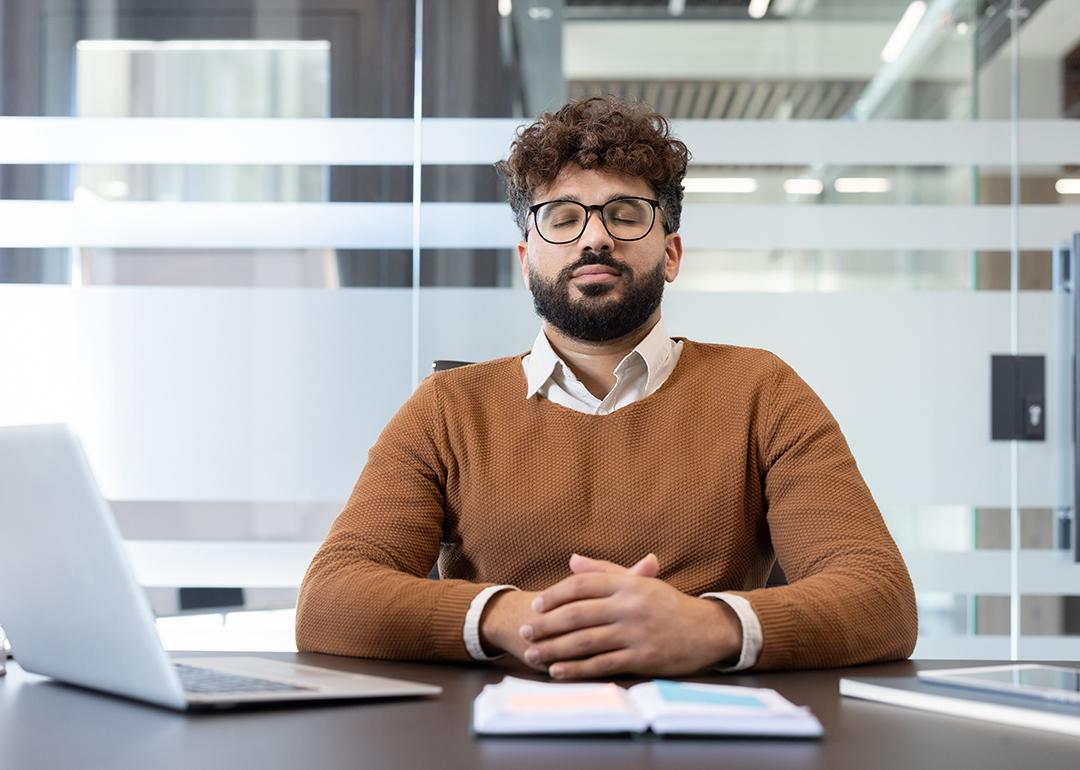 A man with eyes closed meditating at his office desk.
