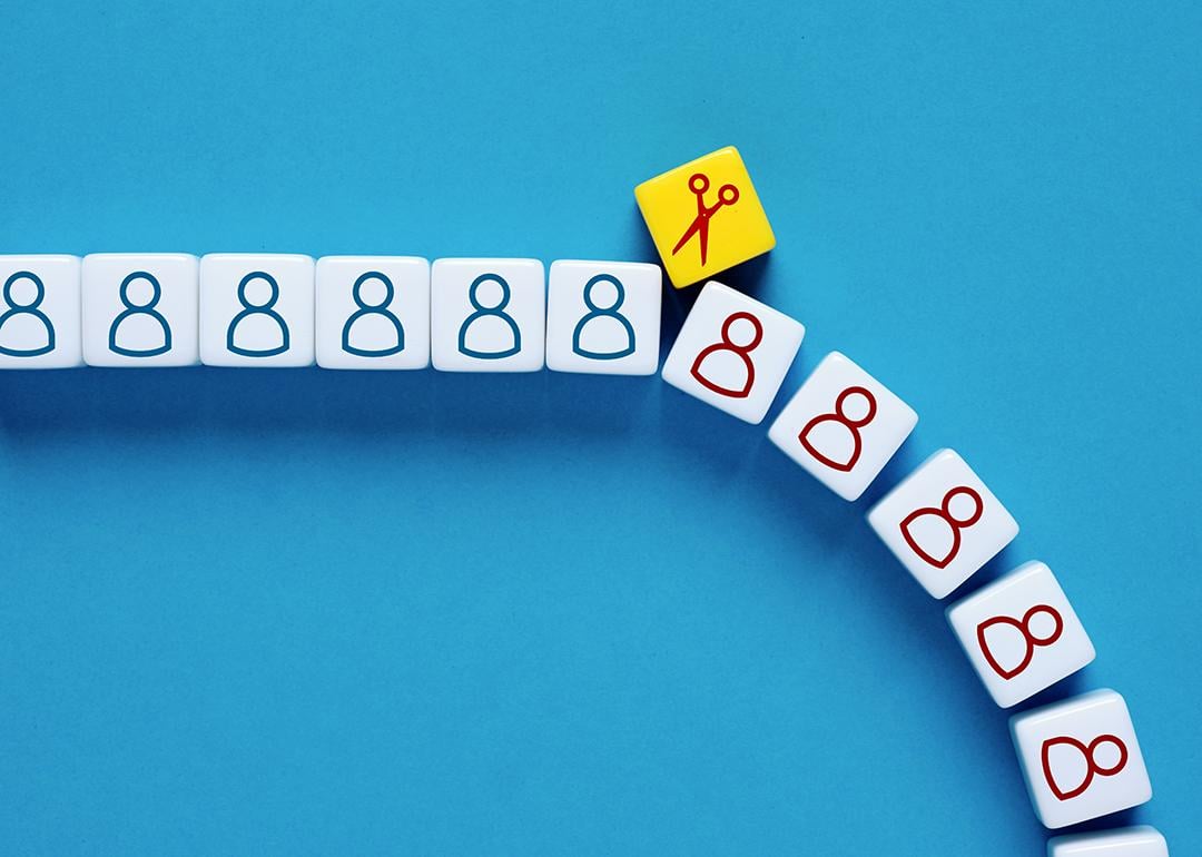 A scissor symbol on a block cutting through a row of human figures as a concept of mass layoffs.