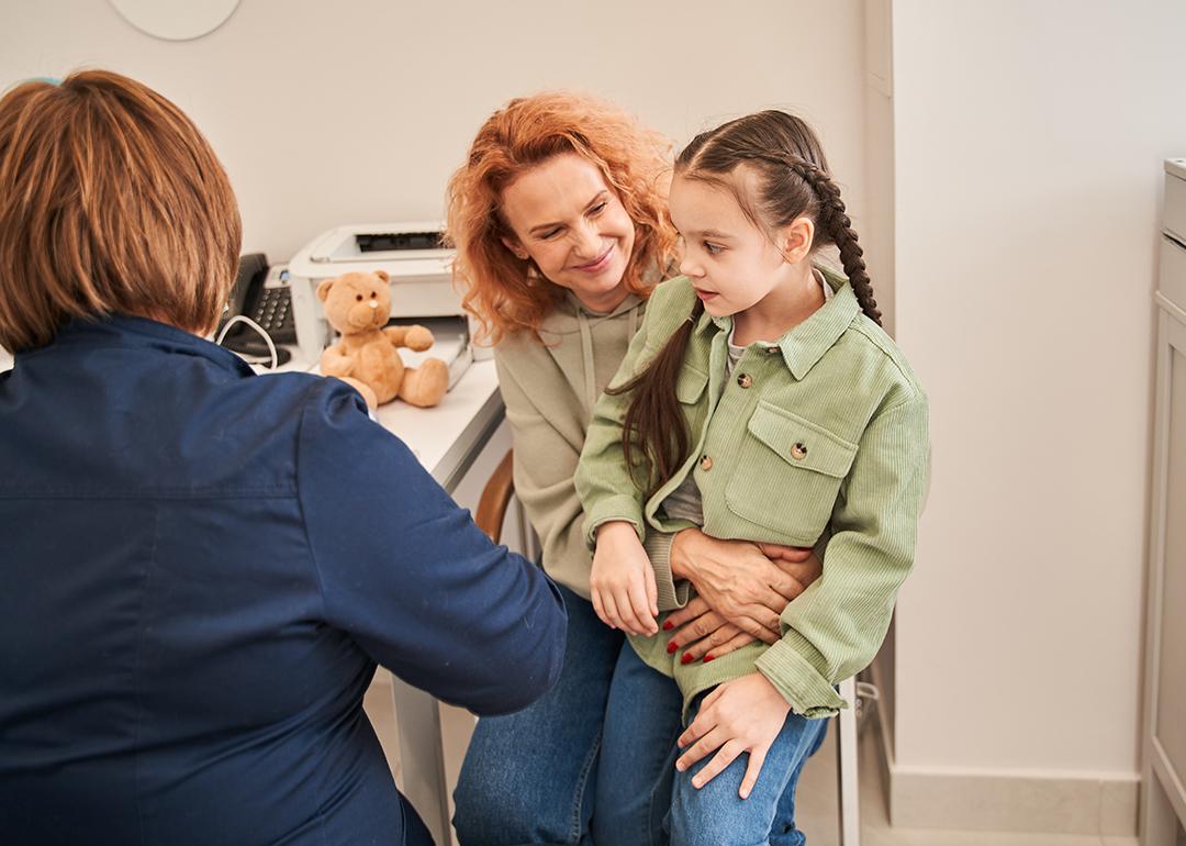 A little girl sitting on her parent's lap during a doctor's consultation.